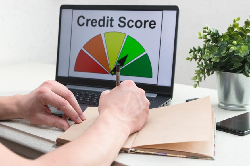 Person writing in notebook.  Graphic of Credit Score on laptop screen