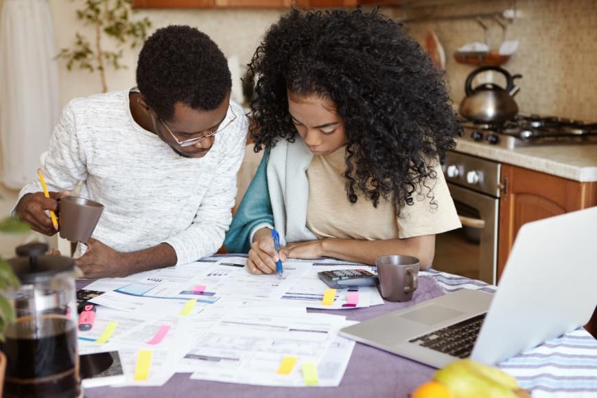 Black couple sitting together and making calculations at a kitchen table covered with papers