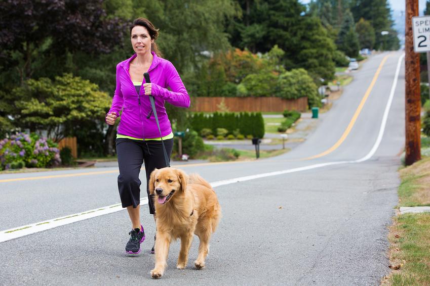 Woman jogging with a dog on a paved road